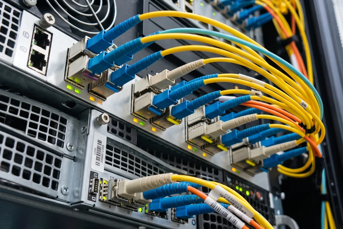 Switch de red con transceptores SFP, conectores LC de fibra óptica azules y patch cords amarillos conectados